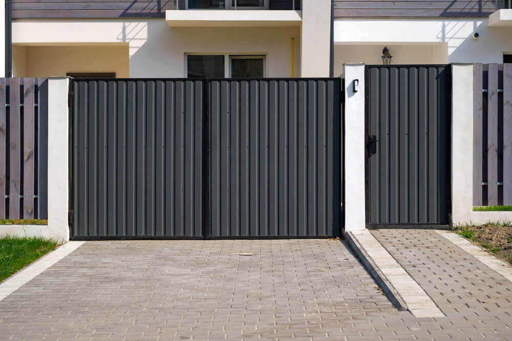 Some dark grey colorbond fencing steel gate with white pillars separating the gates